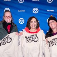 Three people posing for photo in front of backdrop and holding up their custom sweatshirts